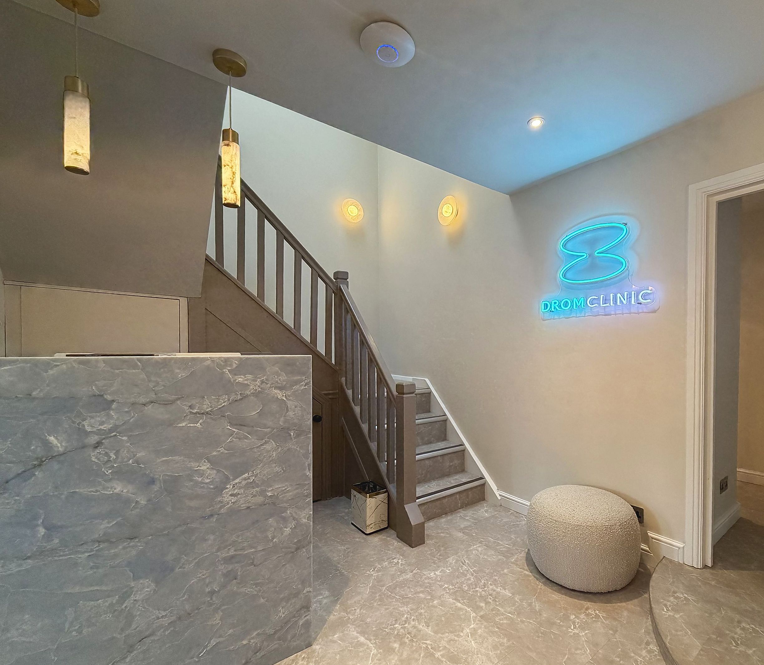 The DROM Clinic reception, with a marble desk, staircase and neon sign